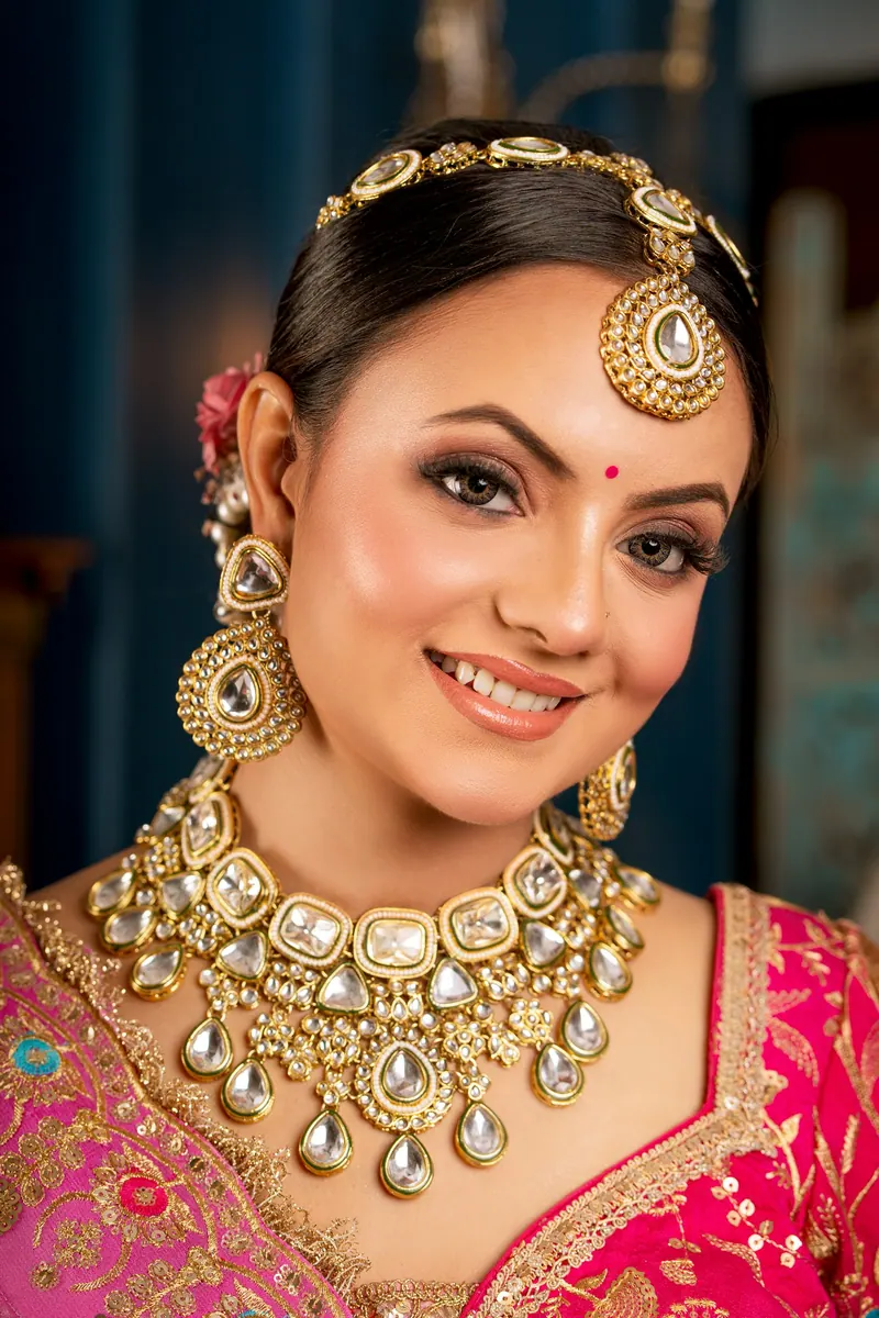 Smiling bride wearing a kundan choker, jhumkas and maang tikka with a pink lehenga