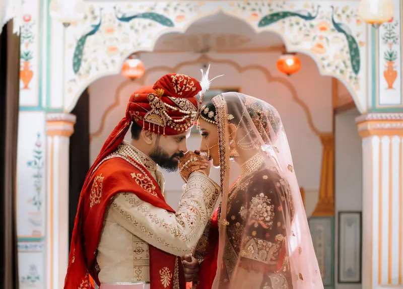 Bride and groom touching foreheads beneath a painted haveli archway in Jaipur