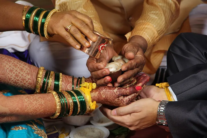 Close-up of hands joined during the kanyadaan ritual, with the bride's green bangles and henna visible