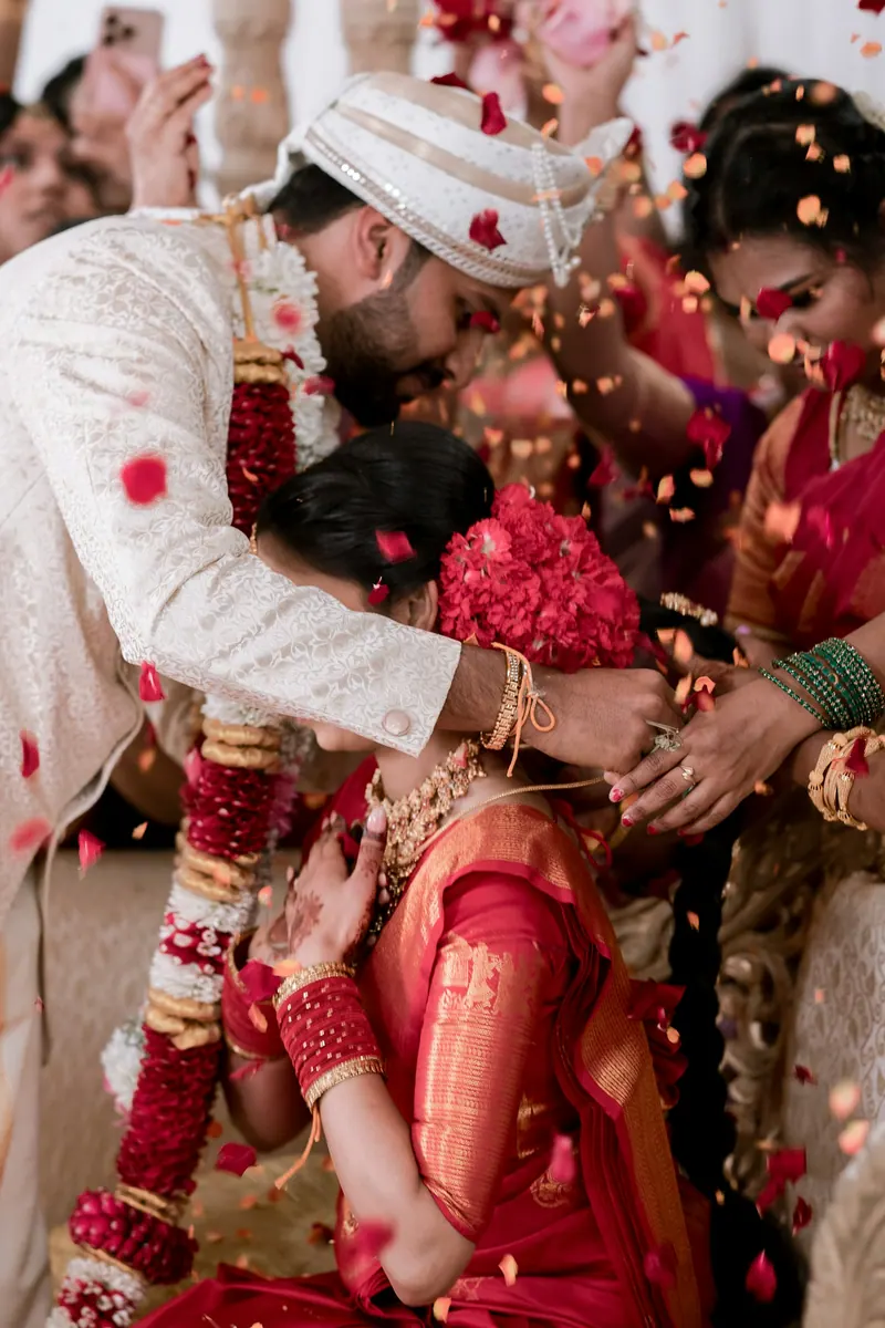 Groom leaning in toward the smiling bride as guests shower them with rose petals during the ceremony