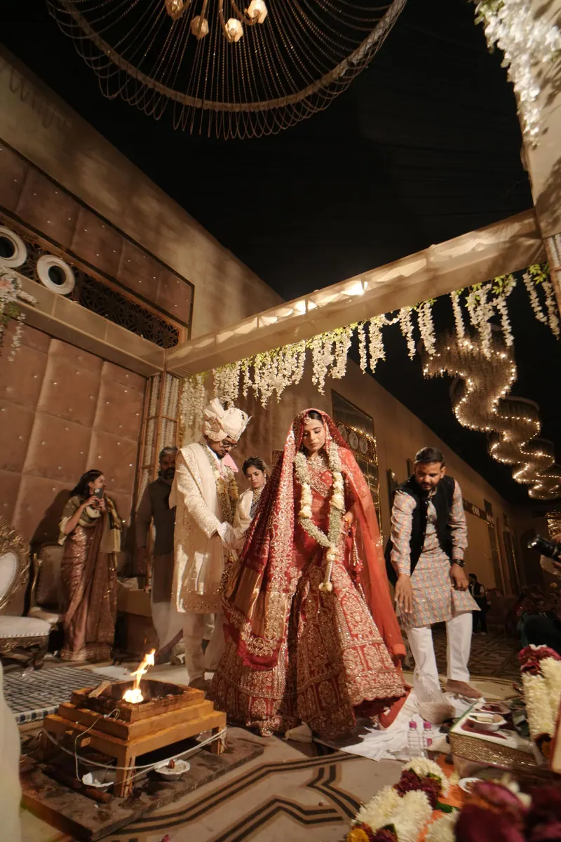 Bride in a red lehenga walking the pheras around the sacred fire in a warmly lit wedding hall in Jaipur