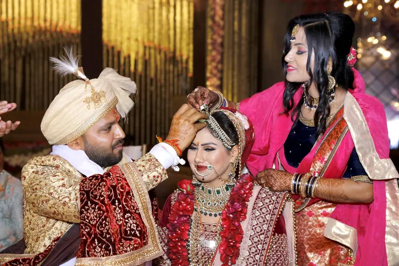 Groom applying sindoor to the bride's hair parting as a relative adjusts her dupatta