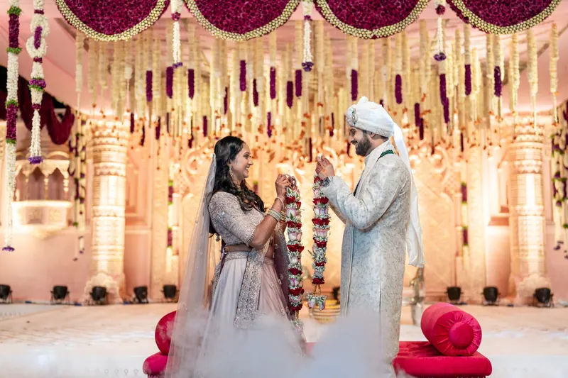 Bride and groom exchanging varmala garlands on a grand pink-and-gold floral stage